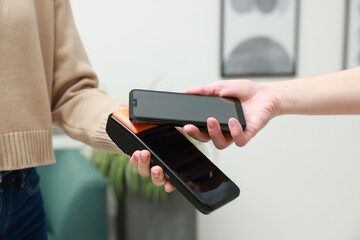 Woman paying for service with smartphone via terminal indoors, closeup