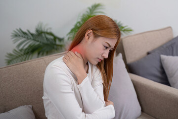 Young woman sitting on sofa, experiencing shoulder pain and self care, reflecting personalized wellness