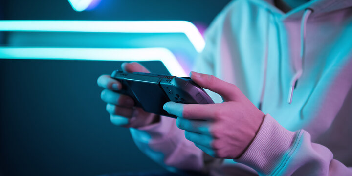 Immersed in Gaming. A young man intensely focuses on a handheld gaming console, illuminated by a vibrant, futuristic blue light.