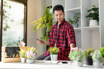 Young man inspecting indoor plants with a tablet, dedicated to enhancing his home gardening experience