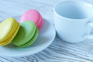 Colorful macaroons and cup of coffee on wooden table, closeup
