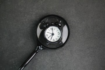 Black alarm clock and magnifying glass on dark background. the concept of finding time. symbolizes...