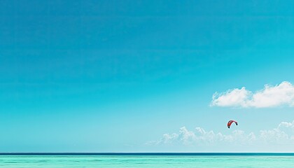 Serene kitesurfing scene; vibrant turquoise ocean under a clear blue sky with a single kitesurfer's kite adding a touch of adventure to the tranquil landscape.
