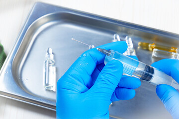 Young doctor in blue gloves, checks the syringe before injection. Close-up.