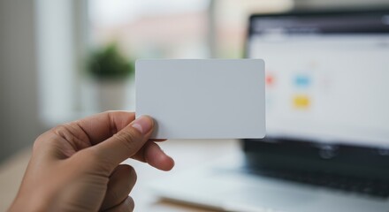 Hand holding blank business card in front of laptop for design mockup