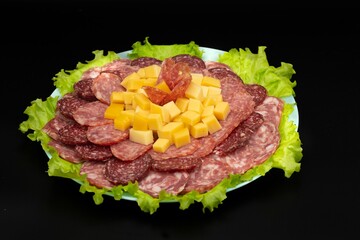 A plate with different types of smoked sausage, cheese and fresh lettuce. Festive cutting.