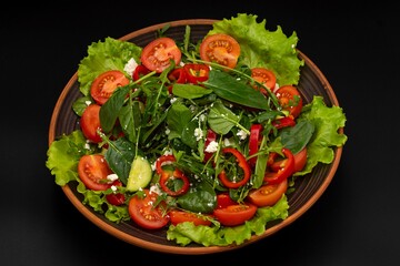 Greek vegetable salad with feta cheese, tomatoes, cucumbers, onions, olive oil on a black background