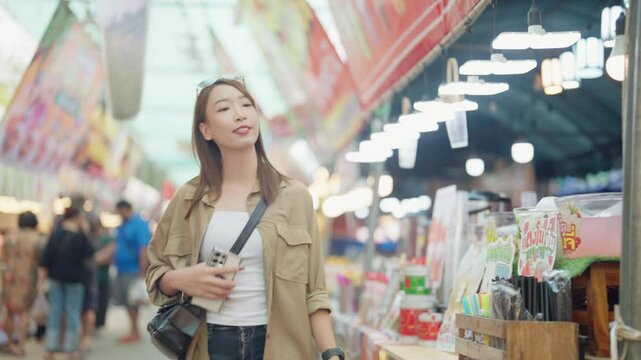A woman is shopping in a market with a crowd of people around her. She is holding a book and a handbag