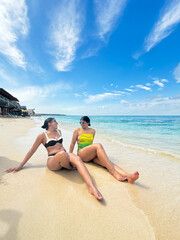 Two women relaxing on tropical beach enjoying summer vacation