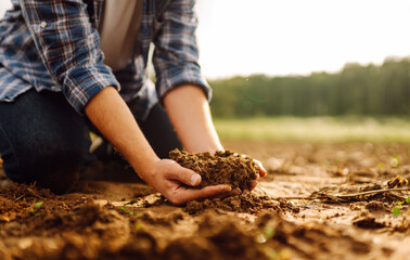 Close up of male hands touching dry ground in an agricultural field. Concept of agribusiness.