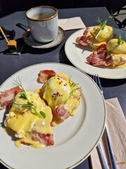Eggs Benedict with ham, topped with hollandaize sauce and served with coffee at a brunch, outside seating, sunlight table, breakfast, top view