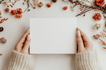 Blank card held in hands surrounded by seasonal decorations and natural elements