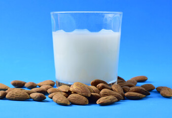 Almond milk, scattered natural almonds and milk in a glass, on a blue background.