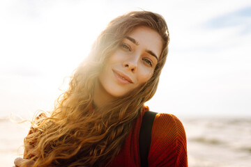 Portrait of a beautiful woman with backpack on the beach in cold weather. Autumn near the sea. Calmness and tranquility. Travel, tourism concept.