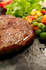 Close up photo of sirloin steak served with vegetables and potatoes on a black platter