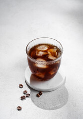 Cold brew coffee in a glass with ice on a light texture background with coffee beans and shadow.