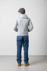 Young boy seen from behind full body with jeans and sweatshirt and woollen cap. Very fashionable casual