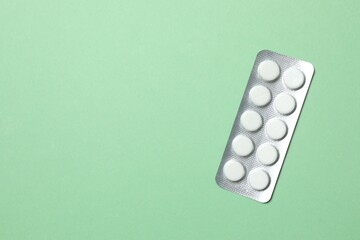 Pills in blister pack on green background, close up