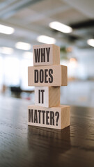 Stacked wooden blocks on a dark surface spell "WHY DOES IT MATTER?" in dark brown sans-serif font. A blurred, bright interior background emphasizes the clean, reflective design.







