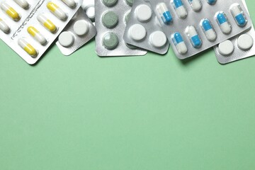 Pills in blister packs on green background, close up