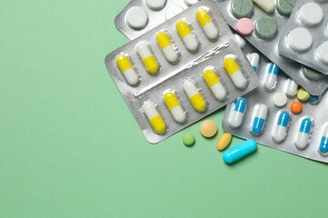 Pills in blister packs on green background, close up