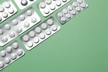 Pills in blister packs on green background, close up
