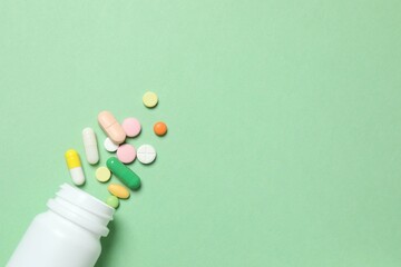 Various pills pouring out of medicine bottle on color background