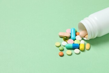 Various pills pouring out of medicine bottle on color background