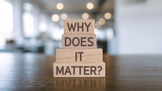 Stacked wooden blocks on a dark surface spell "WHY DOES IT MATTER?" in dark brown sans-serif font. A blurred, bright interior background emphasizes the clean, reflective design.







