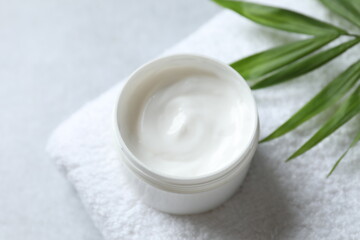 A jar of cream and a palm leaf on a white towel, top view. Professional and beauty products