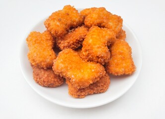 High angle view of fried chicken nuggets in a white plate on a white background. 