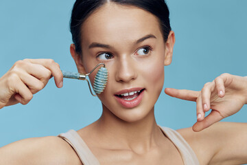 Young woman using a jade roller on her face, showcasing a fresh and glowing complexion against a...