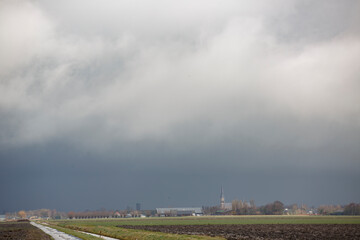 Sneeuwwolken casting dramatic shadows over a rural landscape with distant buildings and moody sky