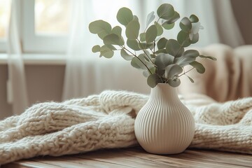 Elegant vase with eucalyptus branches and cozy knitted blanket on table