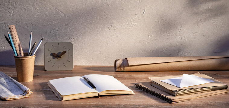 Desk workspace with notebooks, writing tools, and correspondence in sunlight during daytime hours.