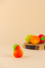 Marzipan candy in the form of a pear on a wooden board on a beige background. Vertical orientation.