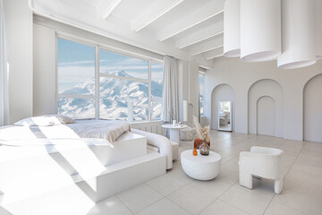 modern pure white interior design of a spacious room features a cozy bed and stylish furniture. Large windows frame a stunning snowy mountain landscape, creating a serene atmosphere during daylight.