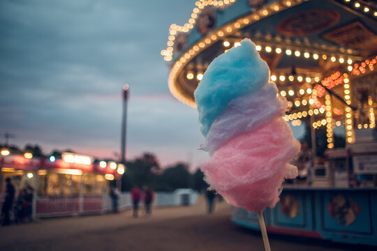 Hand holding fluffy cotton candy at a vibrant carnival during the afternoon. - Powered by Adobe