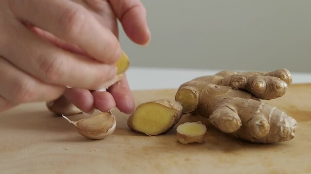 Woman picking up fresh ginger and garlic off wooden cutting board, healthy eating close up