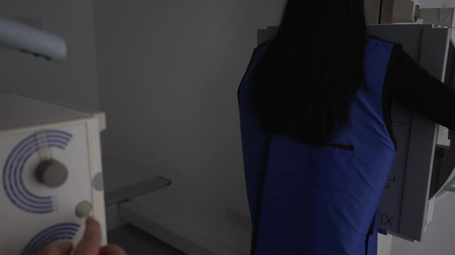 Point of view of a medical technologist operating an x-ray machine on a patient, the patient is wearing a blue protective lead vest.