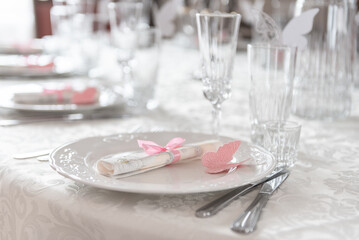 Elegant Table Setting with White Plate and Pink Butterfly Decor. Arrangement featuring a white plate adorned with pink butterfly themed decorations, cutlery, glasses on an elegant white tablecloth