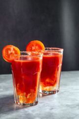 Two vegetable shaken cocktails in glass on dark grey background. Red tomato cocktail. Served with tomato slice. Vegan menu.