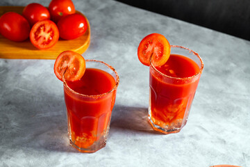 Two vegetable shaken cocktails in glass on dark grey background. Red tomato cocktail. Served with tomato slice. Vegan menu.