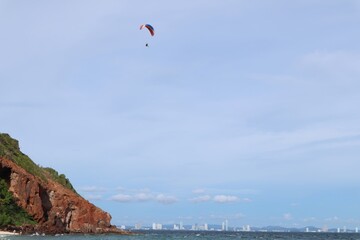 sea A person paragliding over a coastal landscape with distant buildings.