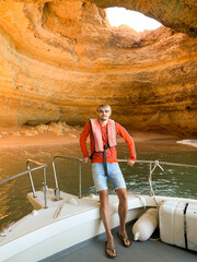 Man standing on boat near coastal cave with golden cliffs and turquoise water