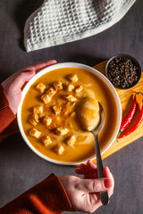 Woman tasting pumkin soup with spoon. Eating cream soup. High angle. Served table with soup bowl, pepper, chili, salt.