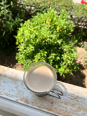 Top view of a glass of coffee on a weathered windowsill with a green garden in the background