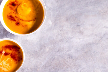 Two bowls with pumpkin soup with paprika spices and cream on white table. Flat lay with copy space. Cream soup. Concept of tasty healthy food.