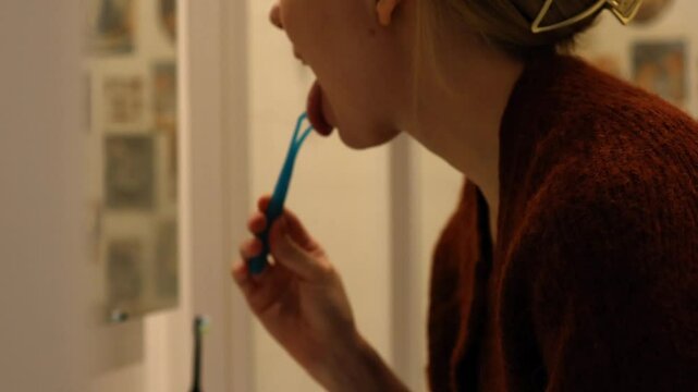 A young man cleans his tongue in the bathroom, demonstrating daily oral hygiene practices in a relaxed personal setting.