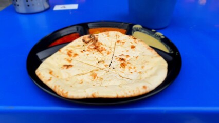 Freshly Made Naan Bread with Colorful Dipping Sauces Served on a Round Plate on a Bright Blue Table Surface in an Outdoor Setting